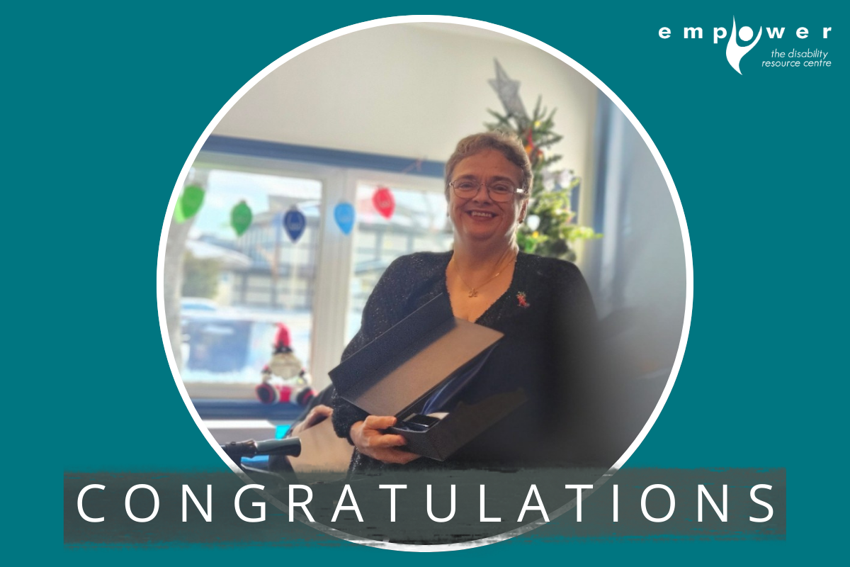 Kimberly Ann Underhay holds her Seniors Award for Independent Living while standing in front of a Christmas tree. Text reads Congratulations! The Empower N L logo is in the upper right corner.